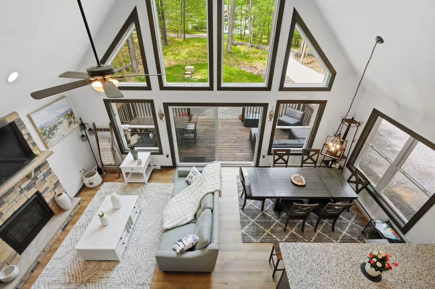 Overhead view of the great room with soaring windows, stone fireplace, dining area and deck beyond